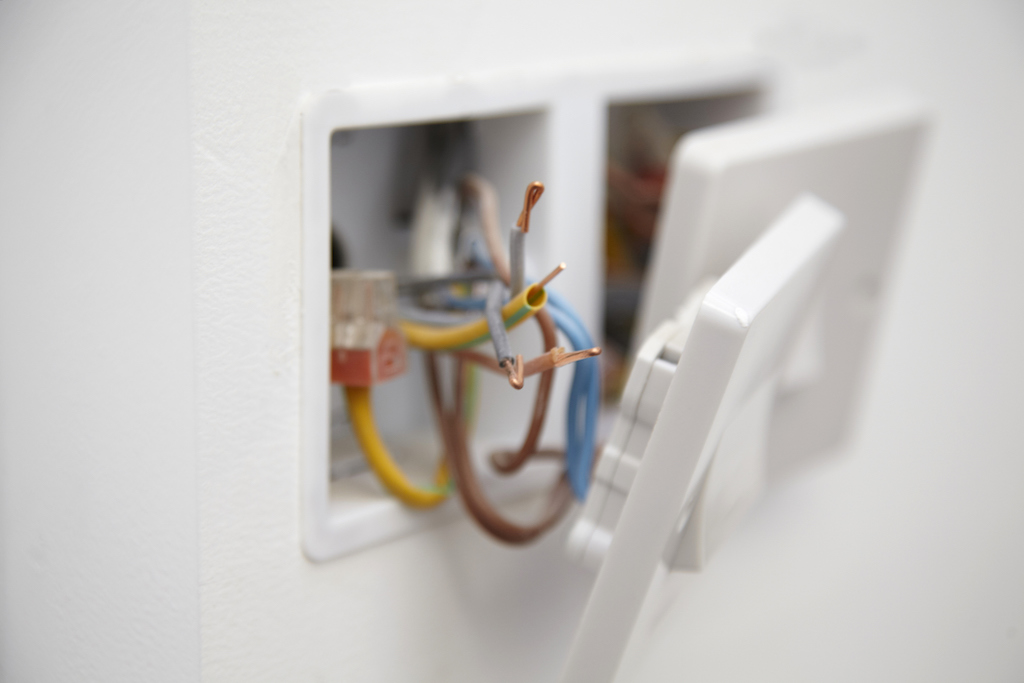 Wiring behind an electrical outlet on white wall.